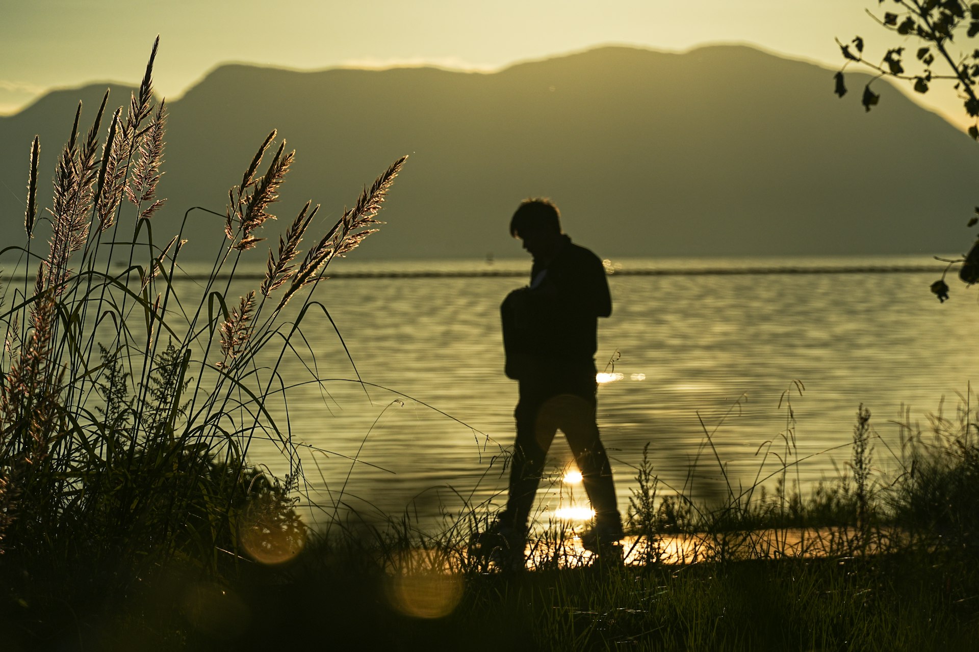 Silhouette of person walking by water at sunset.
